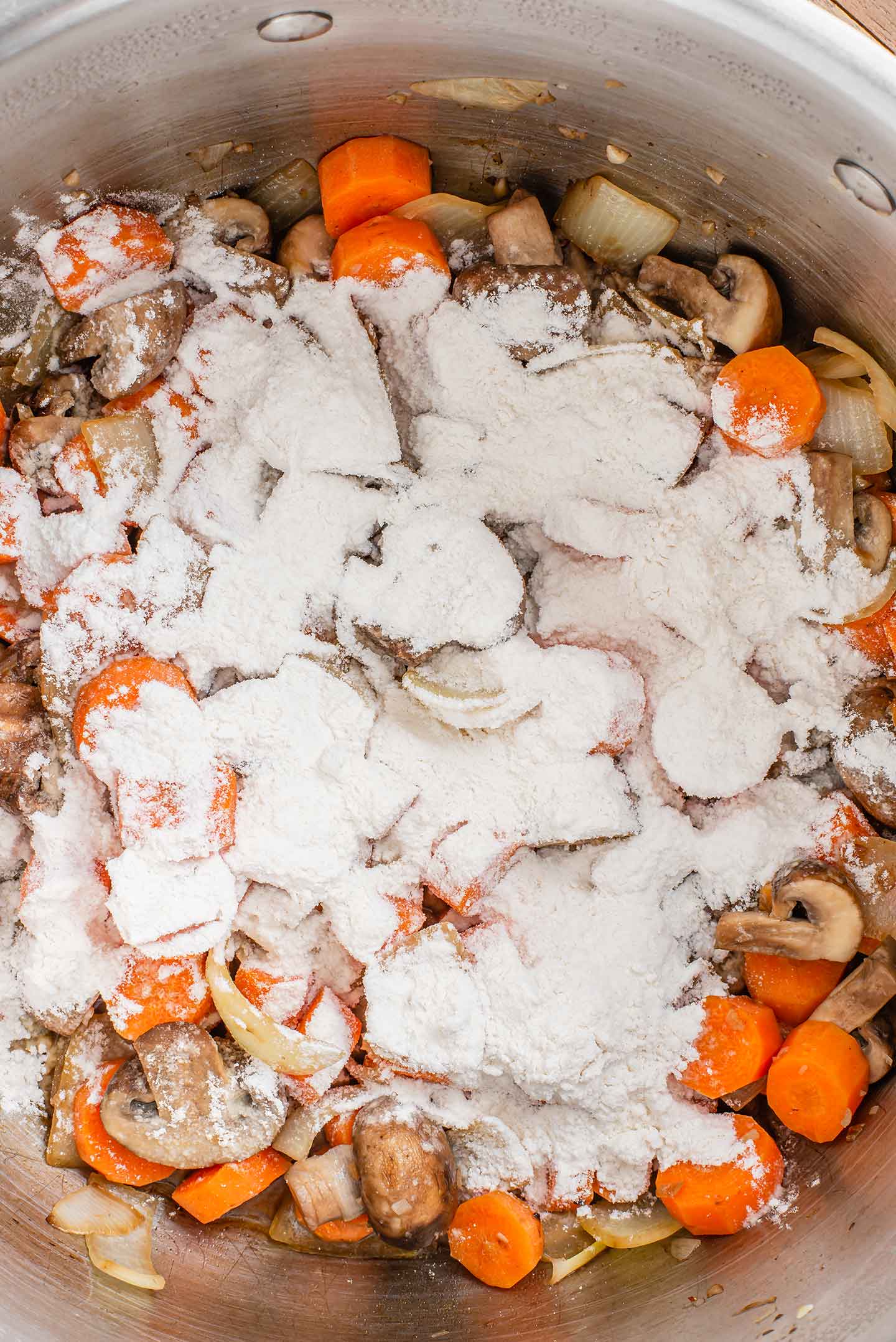 Top down view of flour coating chopped vegetables in a pot.