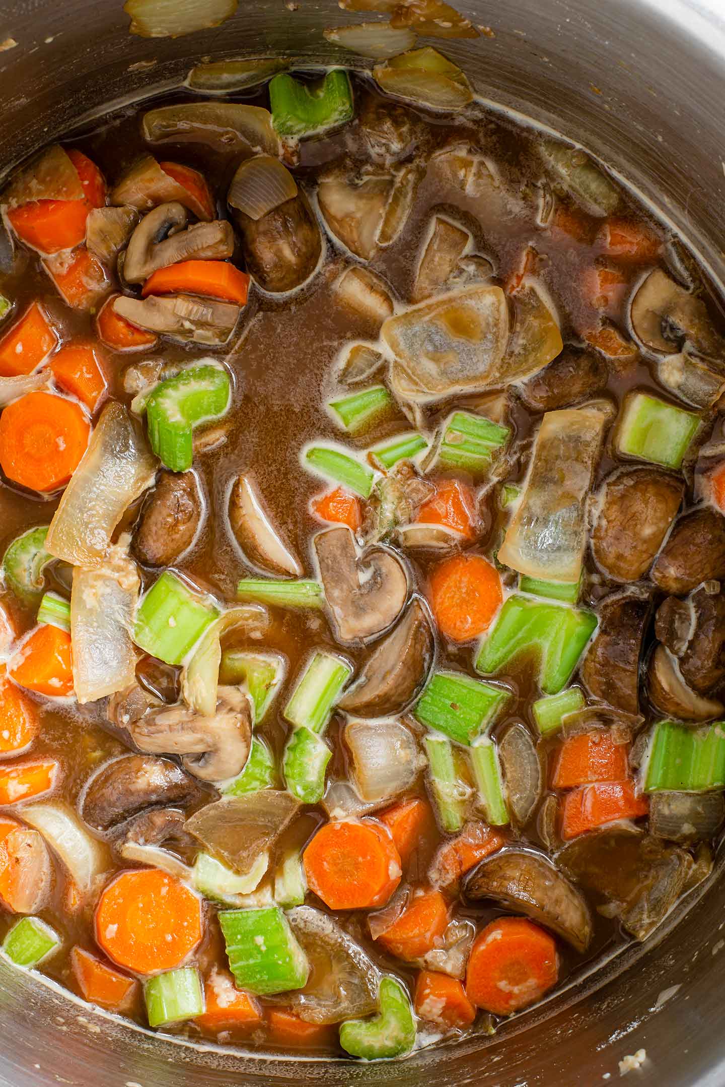 Top down view of Guinness stout added to a pot of chopped vegetables thickened with flour.
