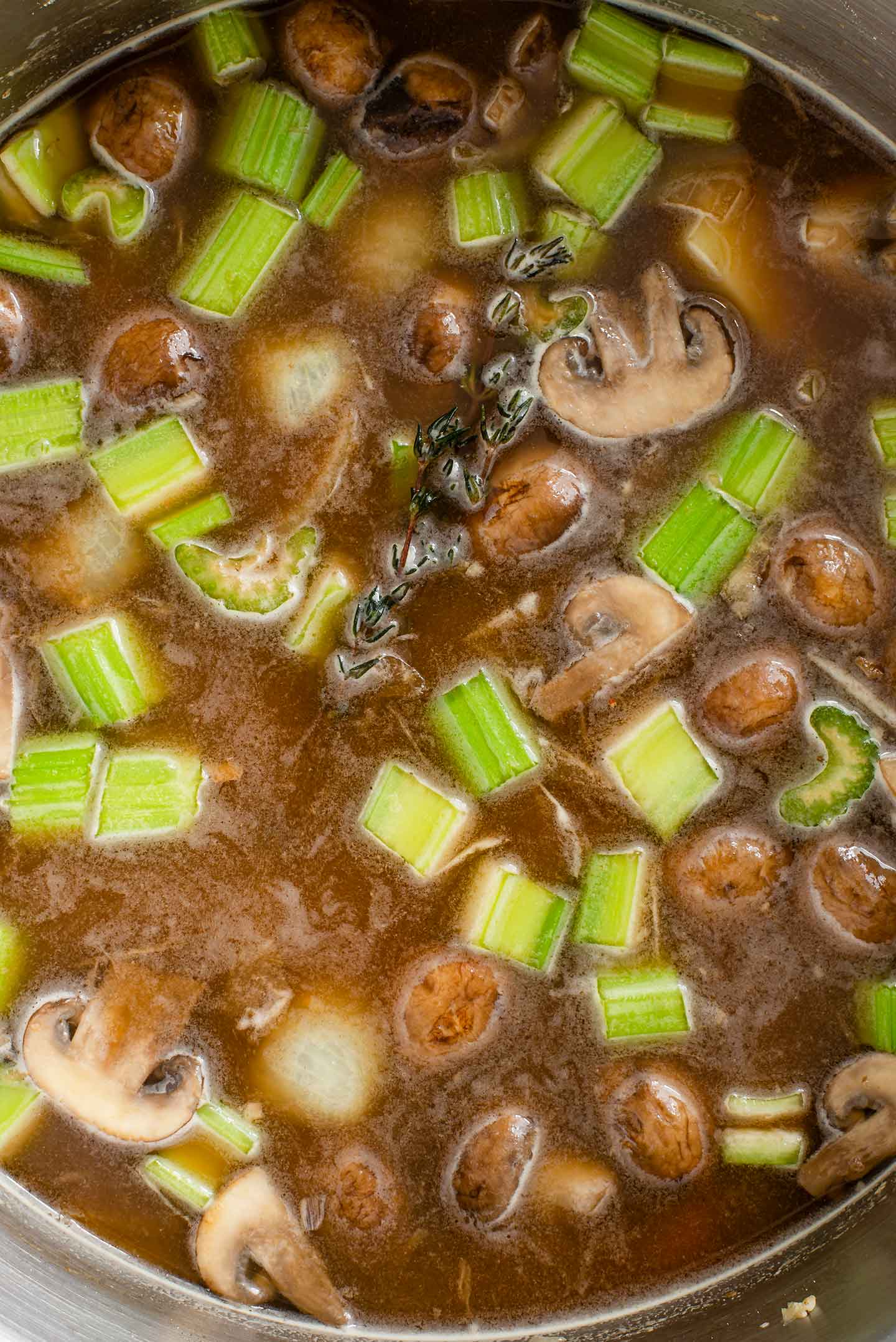 Top down view of chopped vegetables covered with a dark broth. A sprig of thyme floats on top.