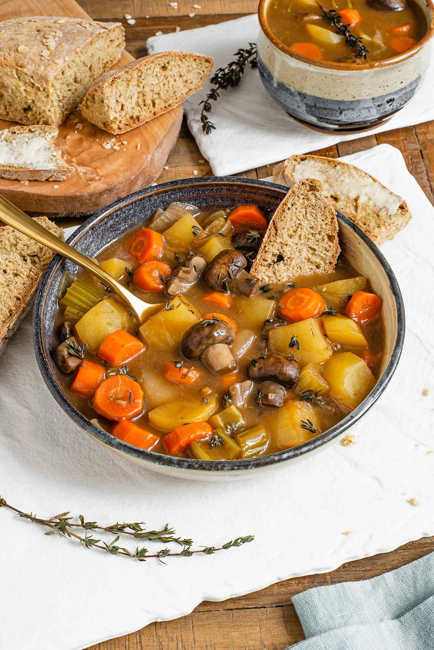 Side view of a slice of Irish soda bread resting in a hearty Guinness stew. A spoon rests between the chunky vegetables.