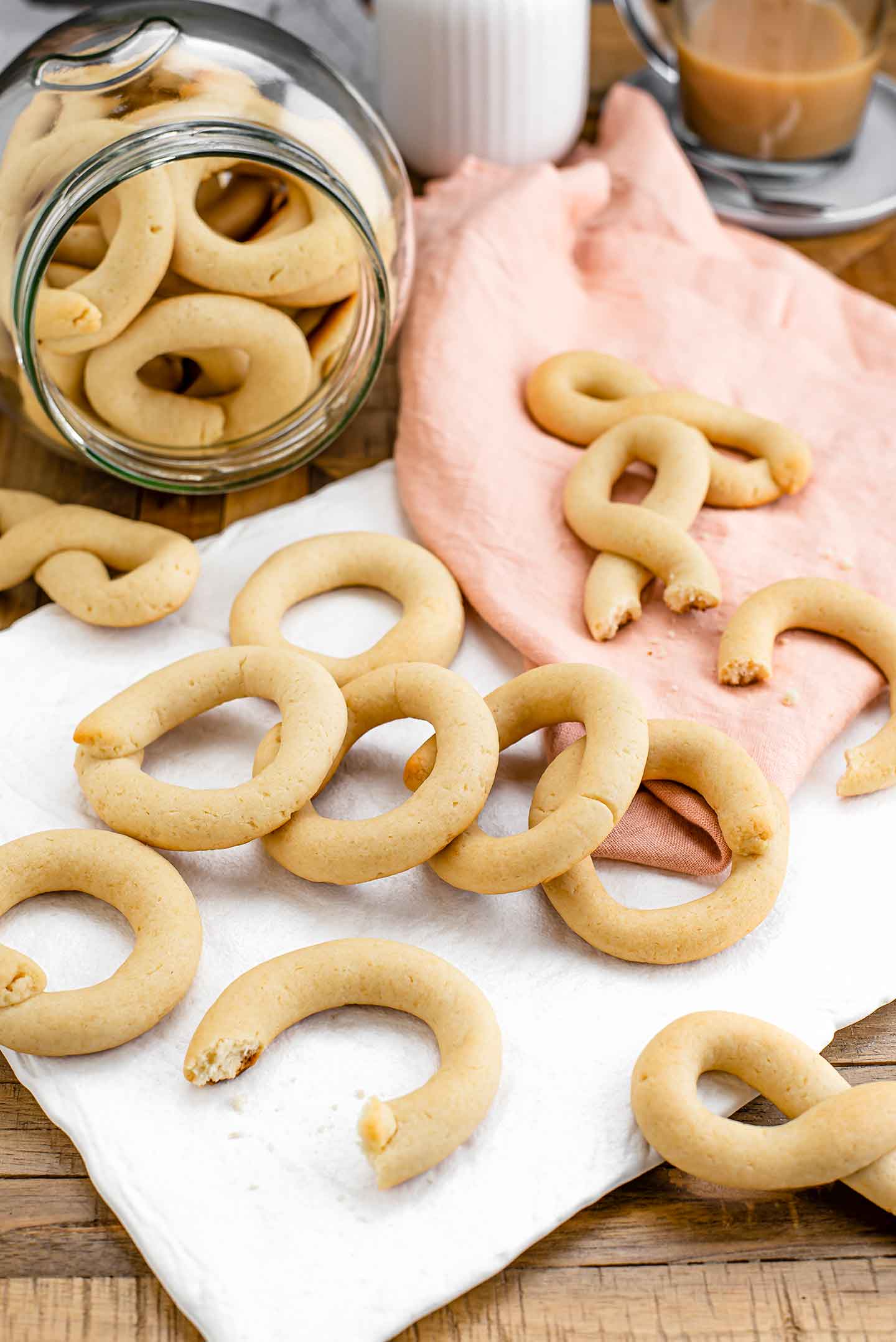 Side view of vegan Portuguese biscoitos spilling out of a cookie jar. Some of the cookies have bites missing revealing their crumbly inside.