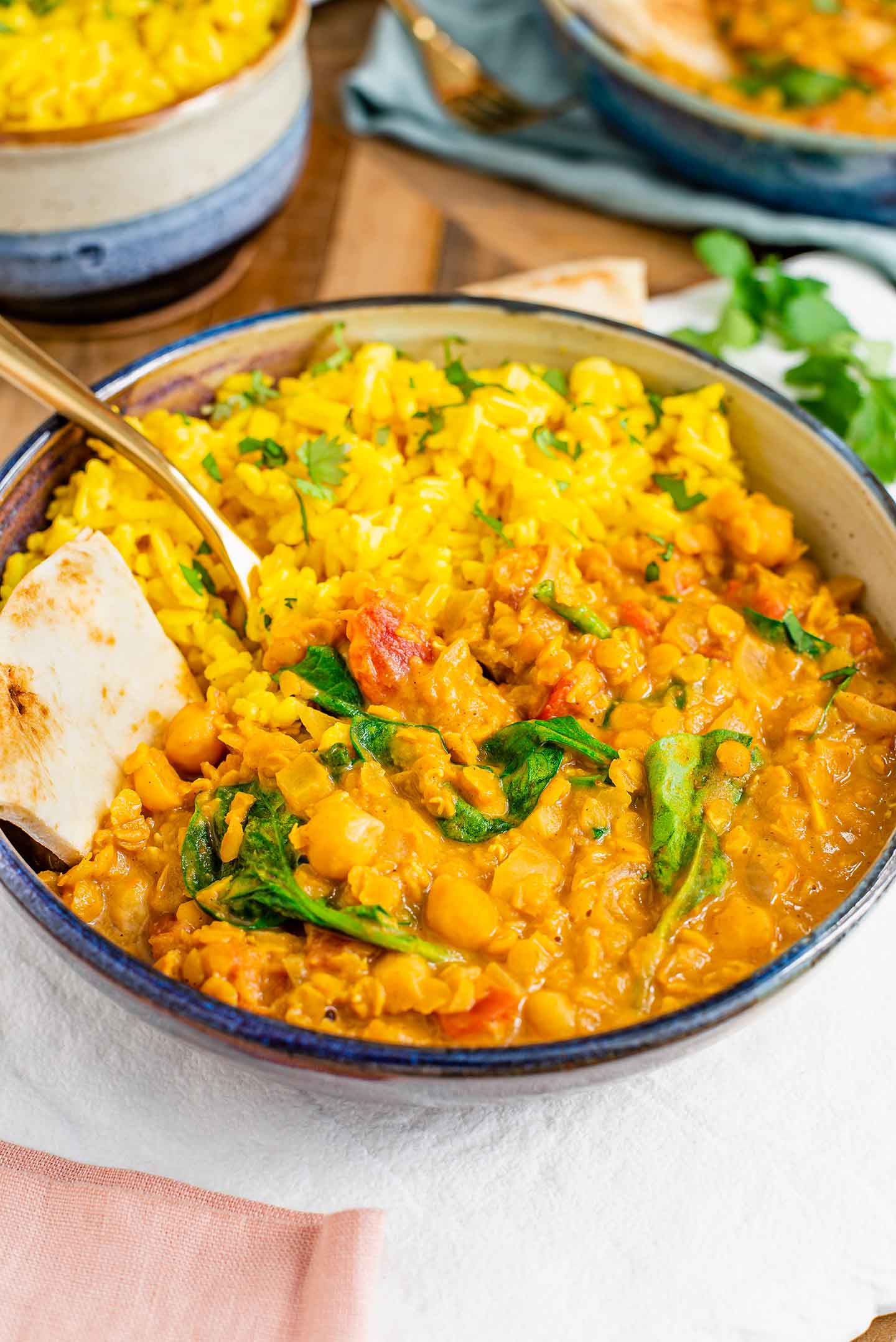 Side view of yellow turmeric rice served on the side of a vegan red lentil curry and naan bread.