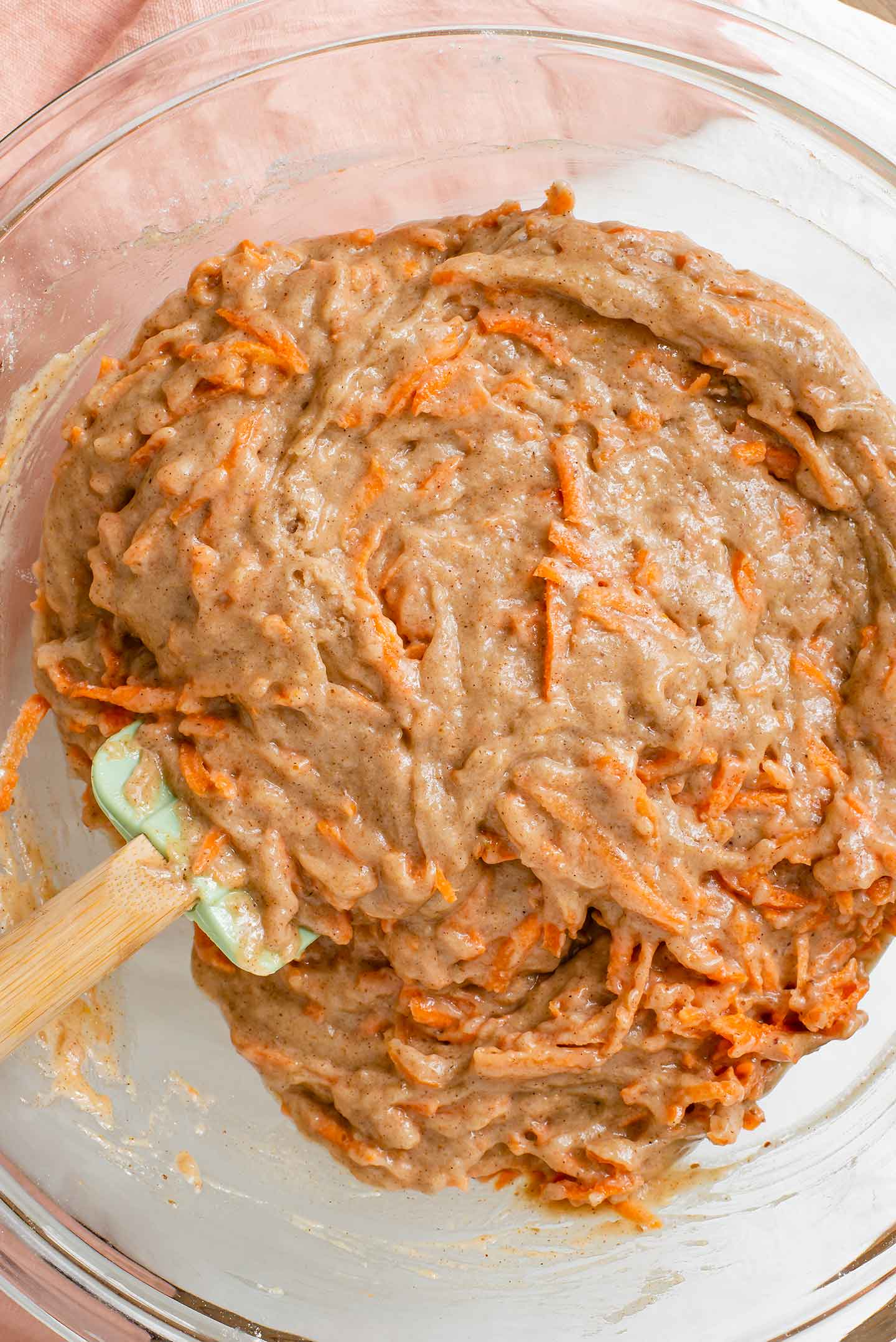 Top down view of a spatula mixing carrots into the cake batter. The batter is thick but moist.