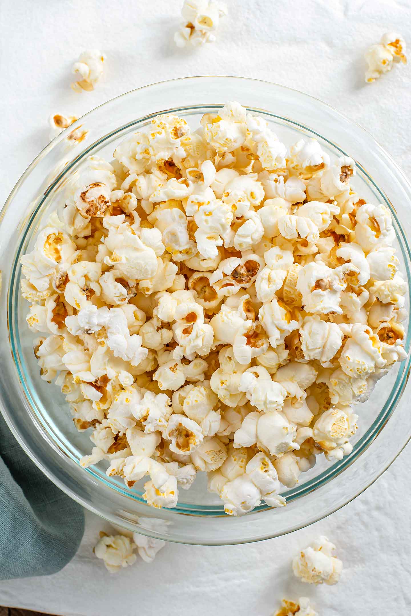 Top down view of white popcorn in a glass bowl. Some fluffy white kernels spill out of the bowl and onto the tray beneath.