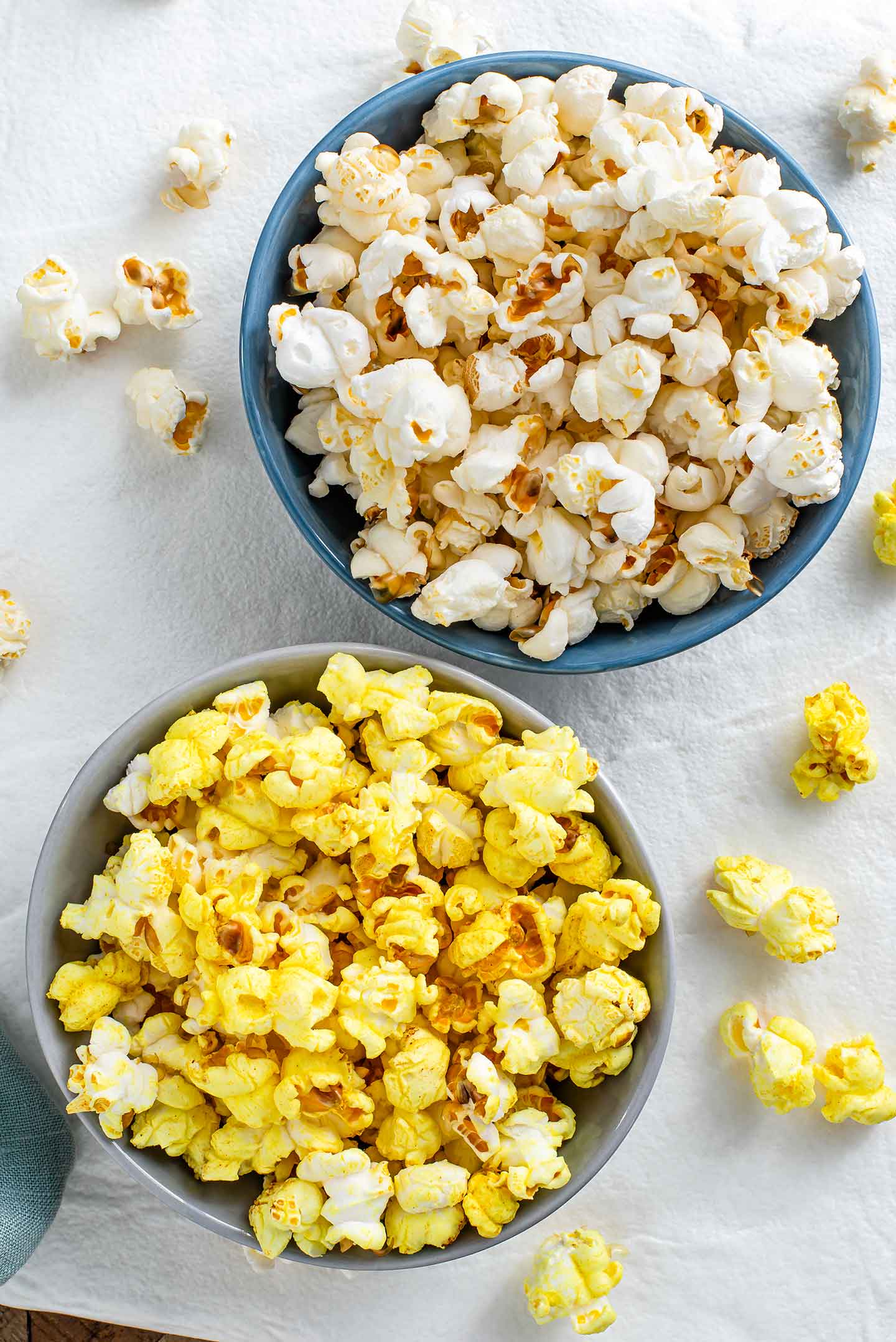 Top down view of two small bowls of popcorn. One bowl has white popcorn and the popcorn in the other bowl is a buttery yellow colour.