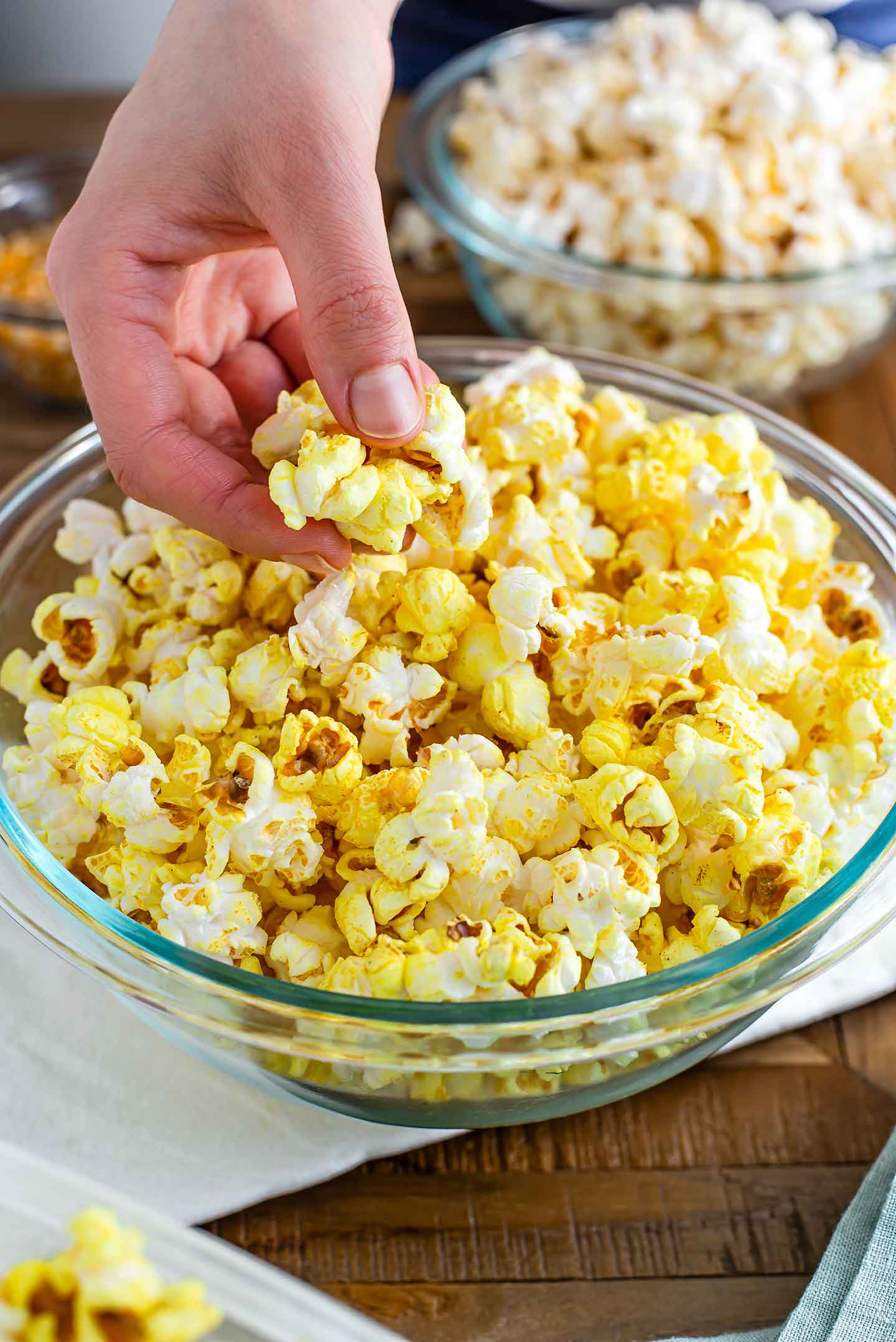 Side view of a hand grabbing popcorn from a large bowl.