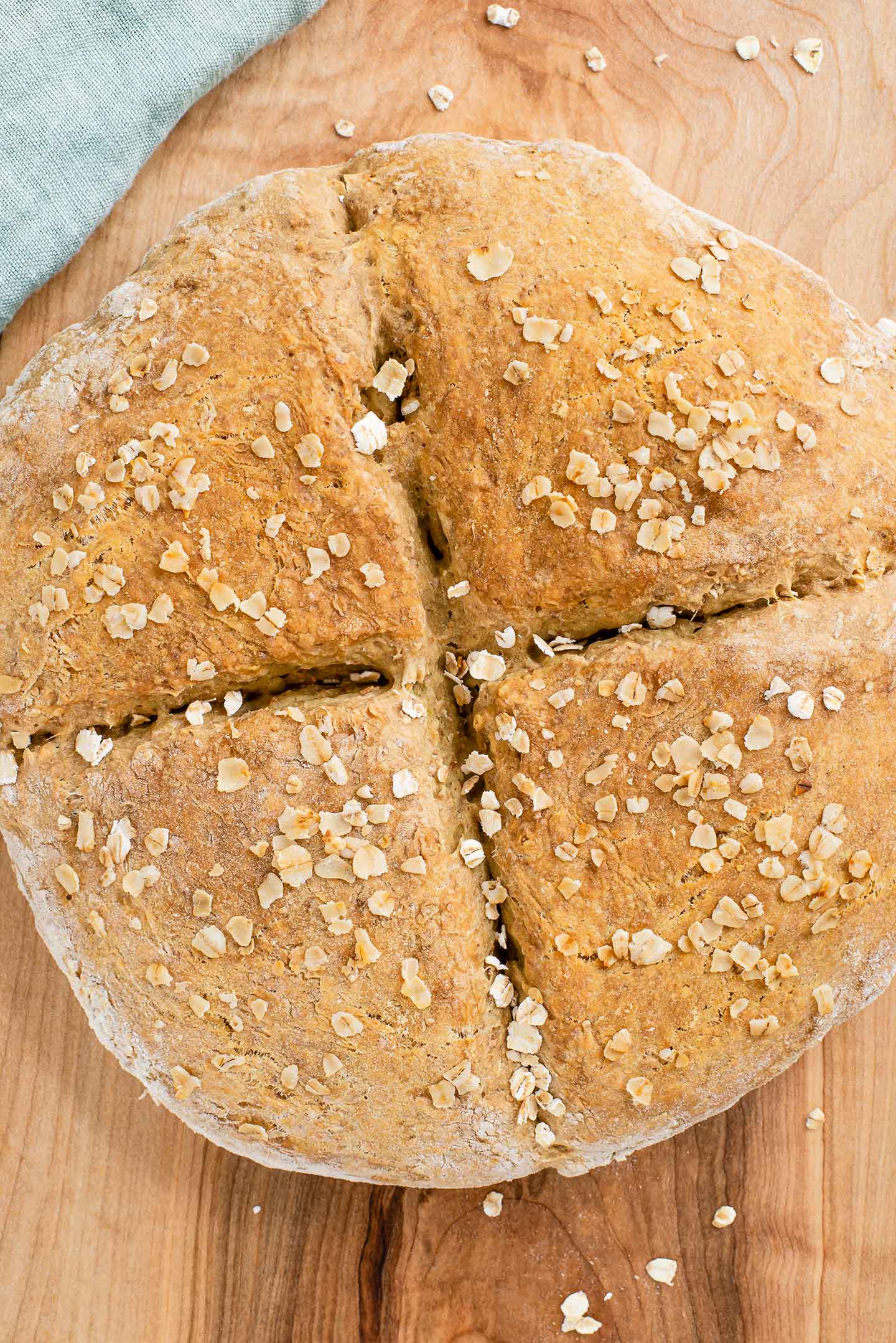 Top down view of a round vegan Irish soda bread loaf with a deep cross. The loaf is sprinkled with oats.