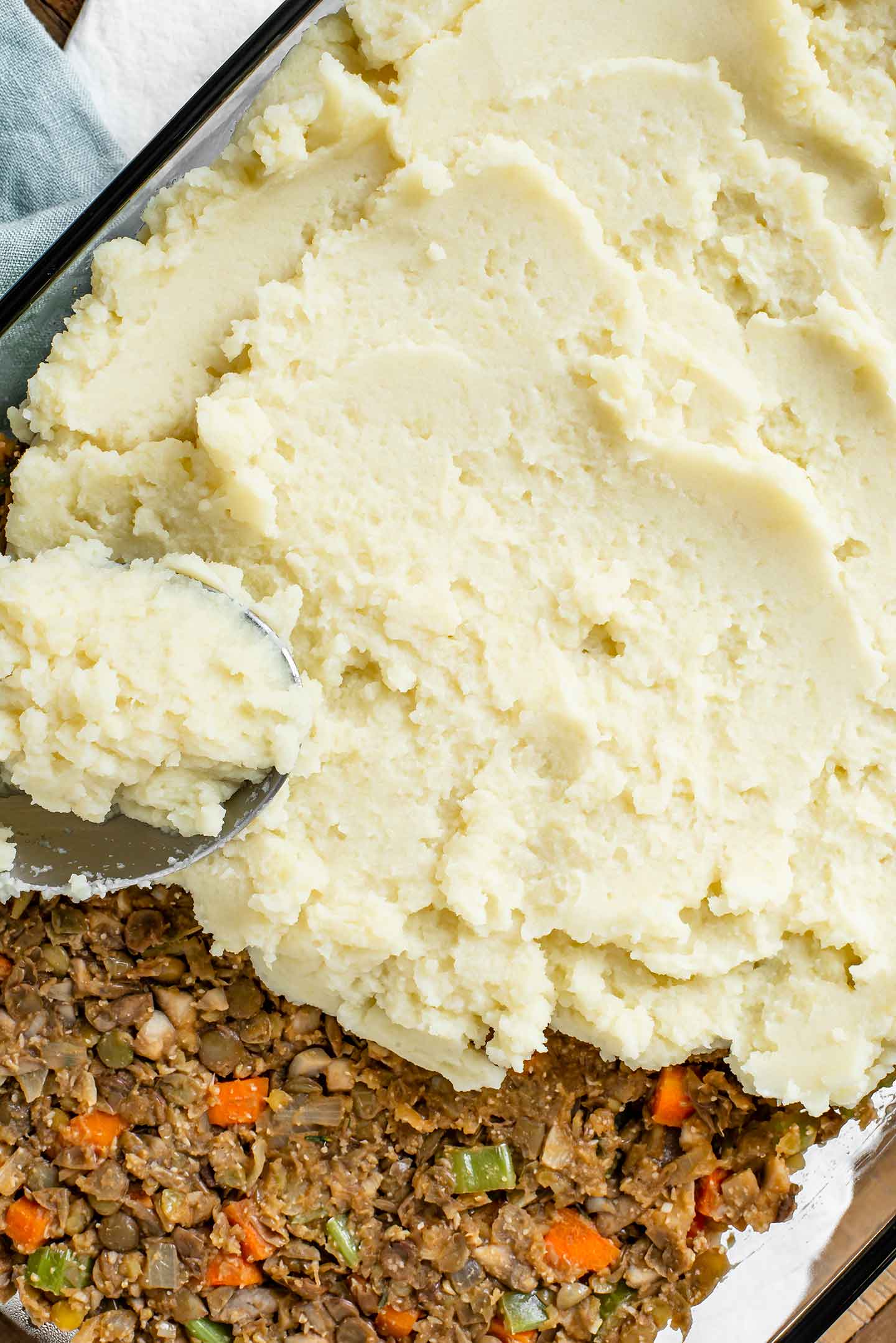 Top down view of mashed potatoes being spread over the lentil and vegetable base in a serving dish.