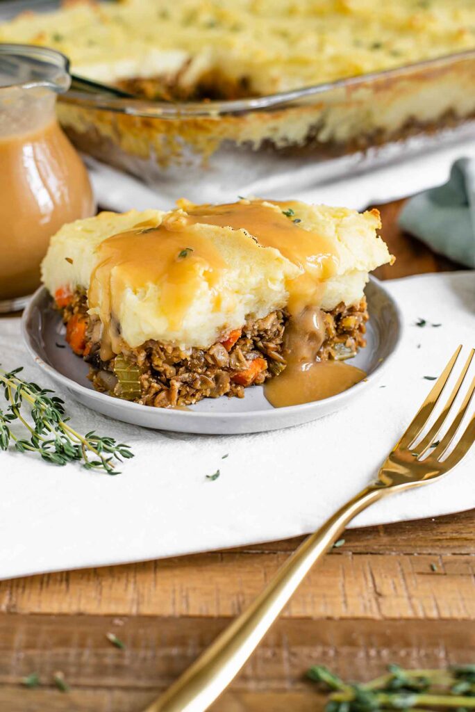 Side view of gravy poured over a slice of lentil shepherd's pie. Golden mashed potatoes top a sturdy lentil vegetable base.