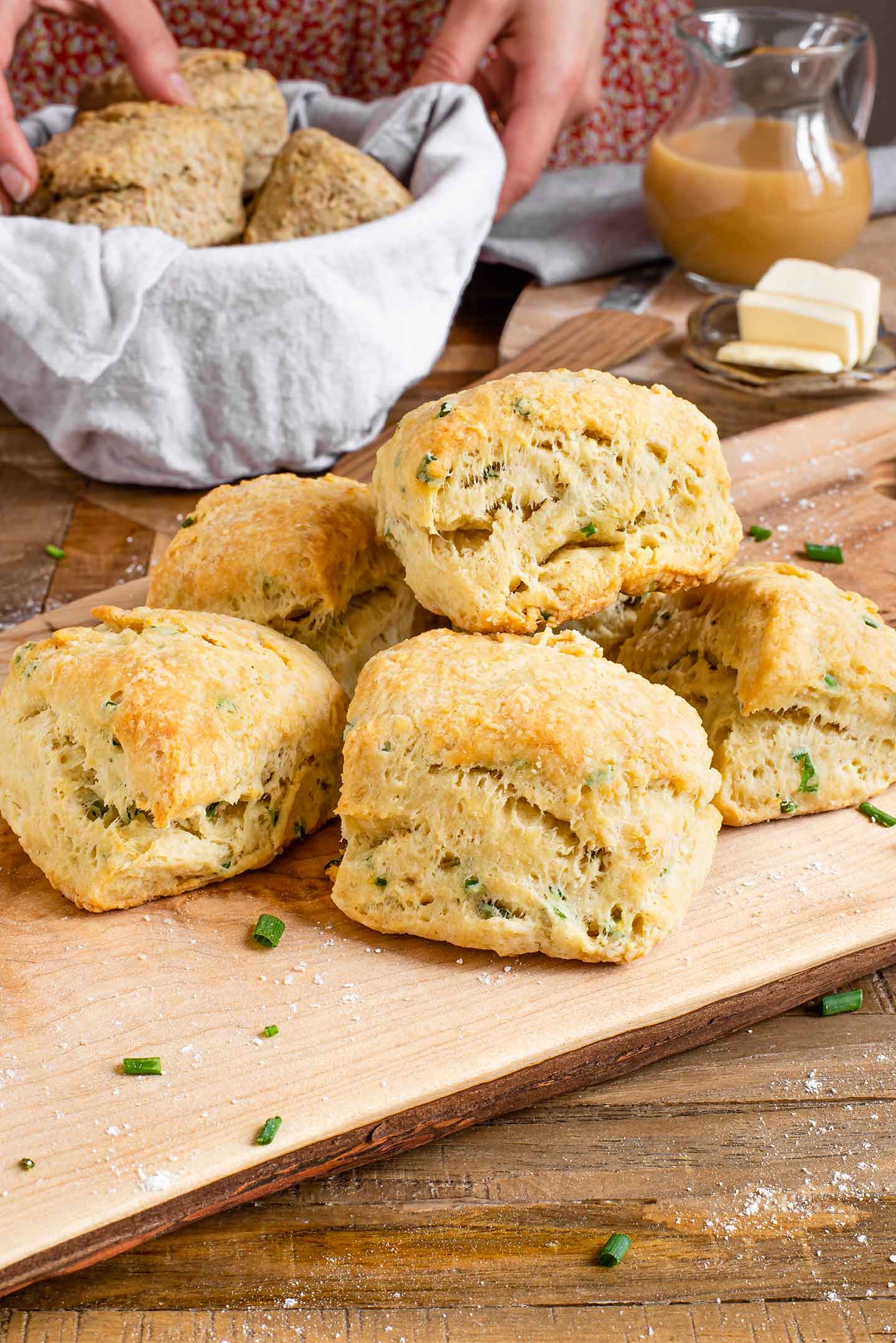 Side view of flaky vegan biscuits piled on top of each other. The biscuits are golden and the layers are visibly pulling away from each other. Fresh chives are speckled throughout the biscuits.