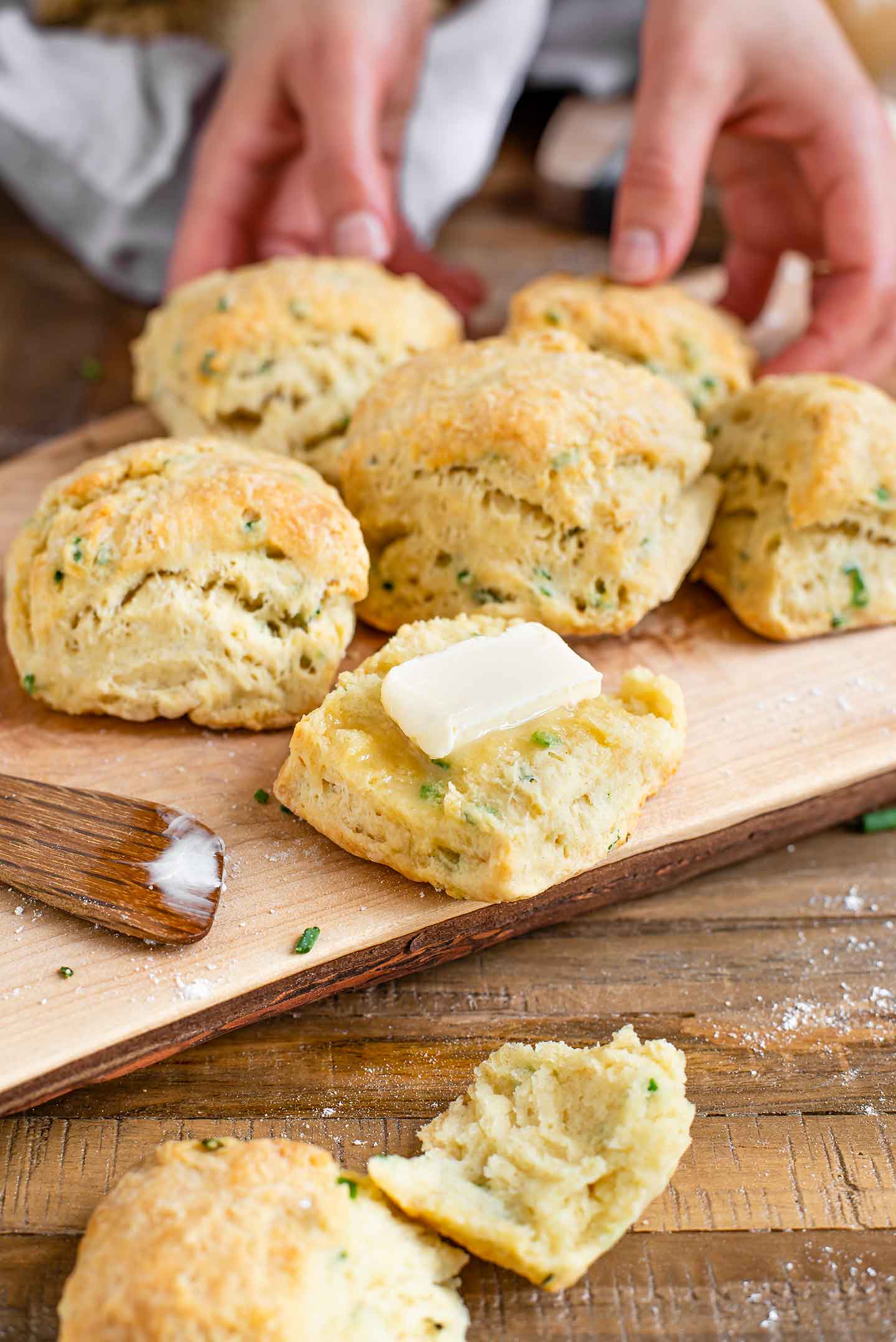 The bottom half of a garlic and chive flaky biscuit has a pat of butter melting into the warm biscuit.