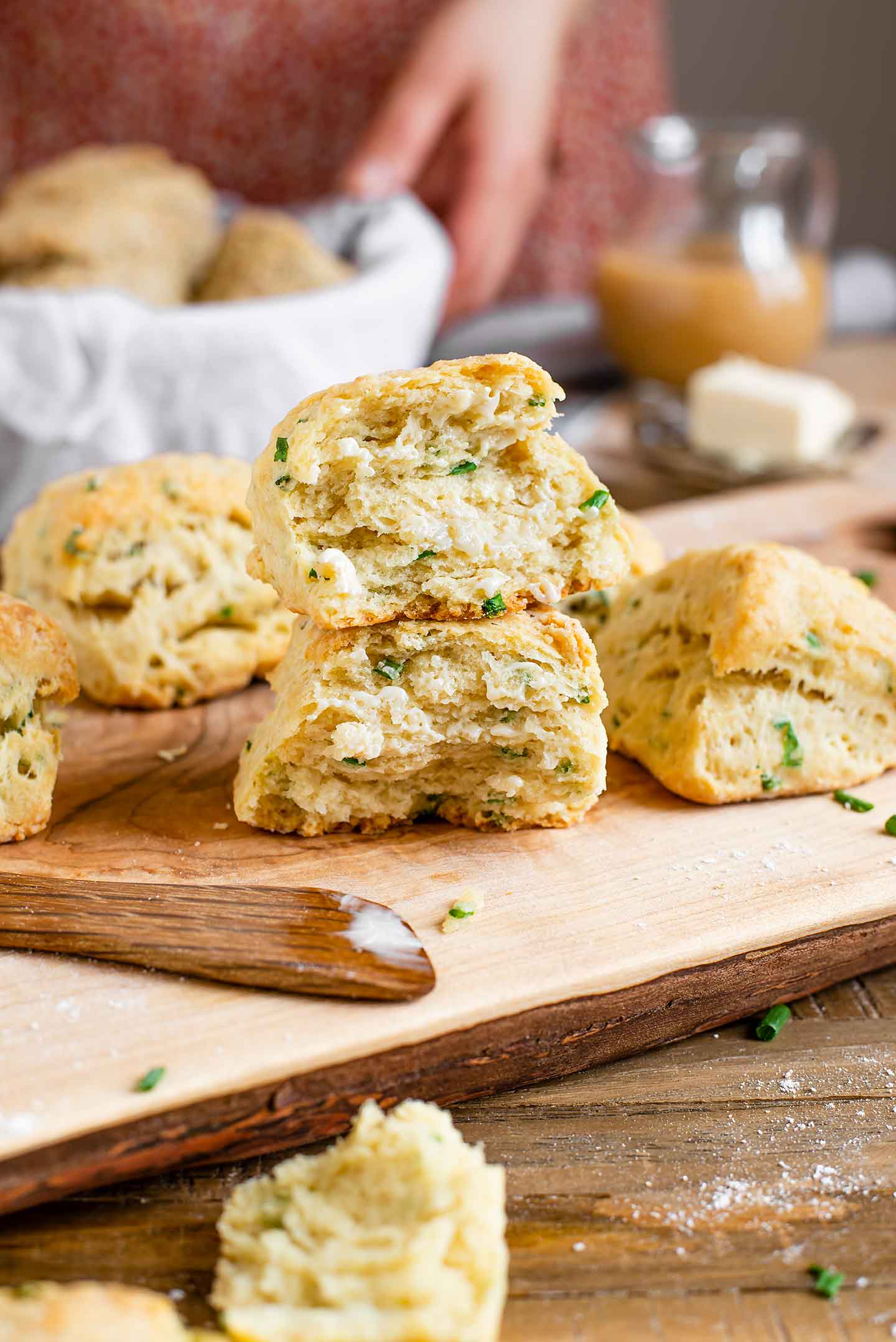 Two halves of a flaky vegan biscuit rest on top of one another to show the layered texture. The biscuit is golden on top and speckled with chives.