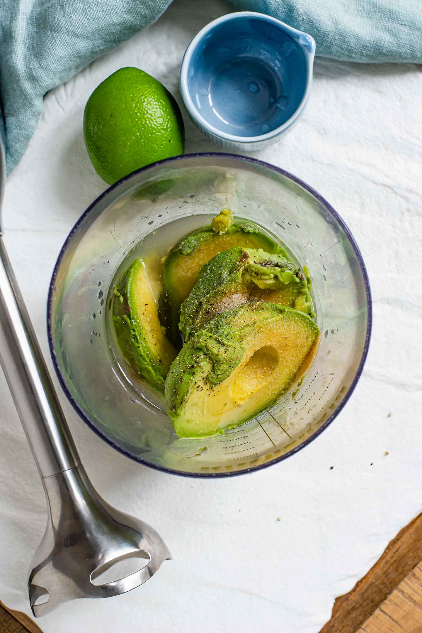 Top down view of the flesh of an avocado in the cup of an immersion blender. The blender lays next to the cup of ingredients. 