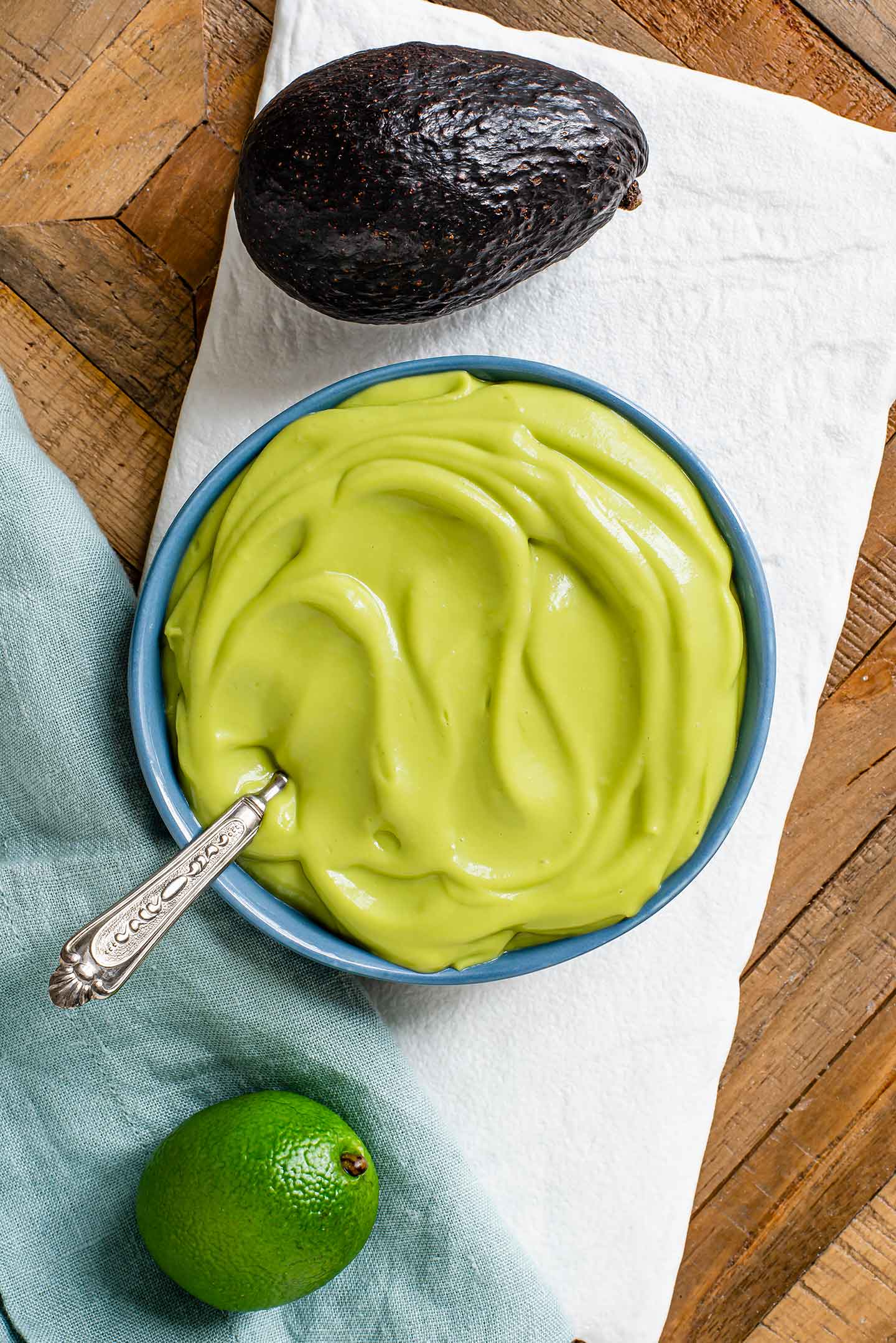 Top down view of a green avocado lime dressing in a small bowl atop a white tray. An avocado and a fresh lime lay next to the bowl.