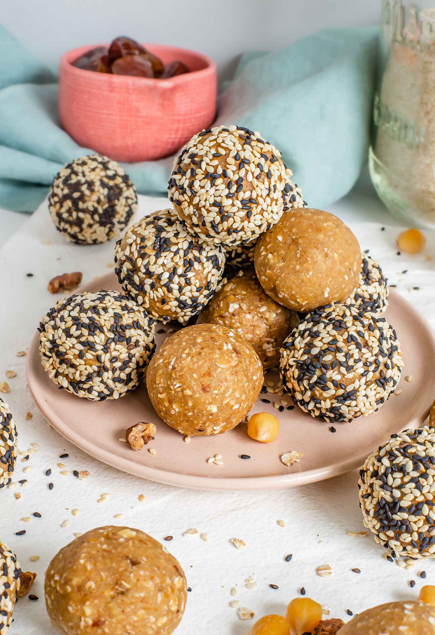 Side view of chickpea tahini protein balls stacked on a small plate. Some balls are rolled in sesame seeds and others have been left without a coating.