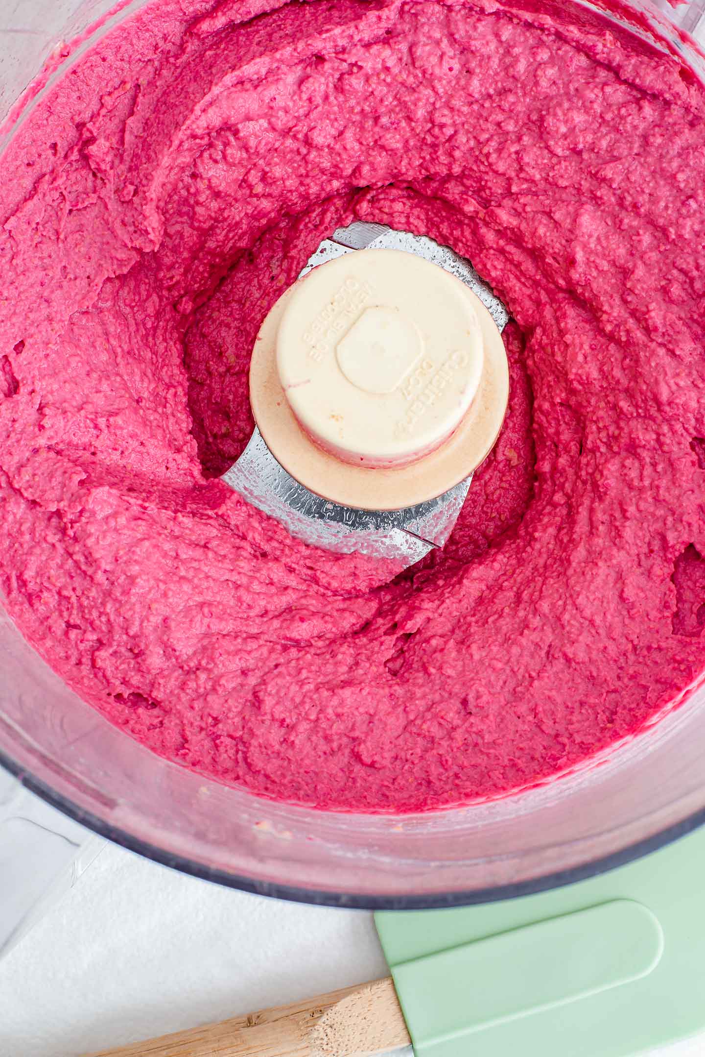 Top down view of bright pink hummus in the bowl of a food processor.