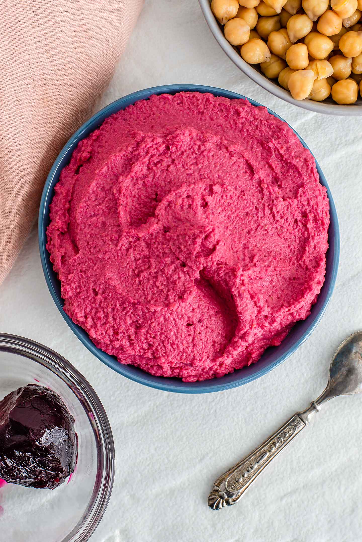 Top down view of beet hummus in a bowl. Cooked chickpeas and a roasted beet fill bowls on either side of the dip.