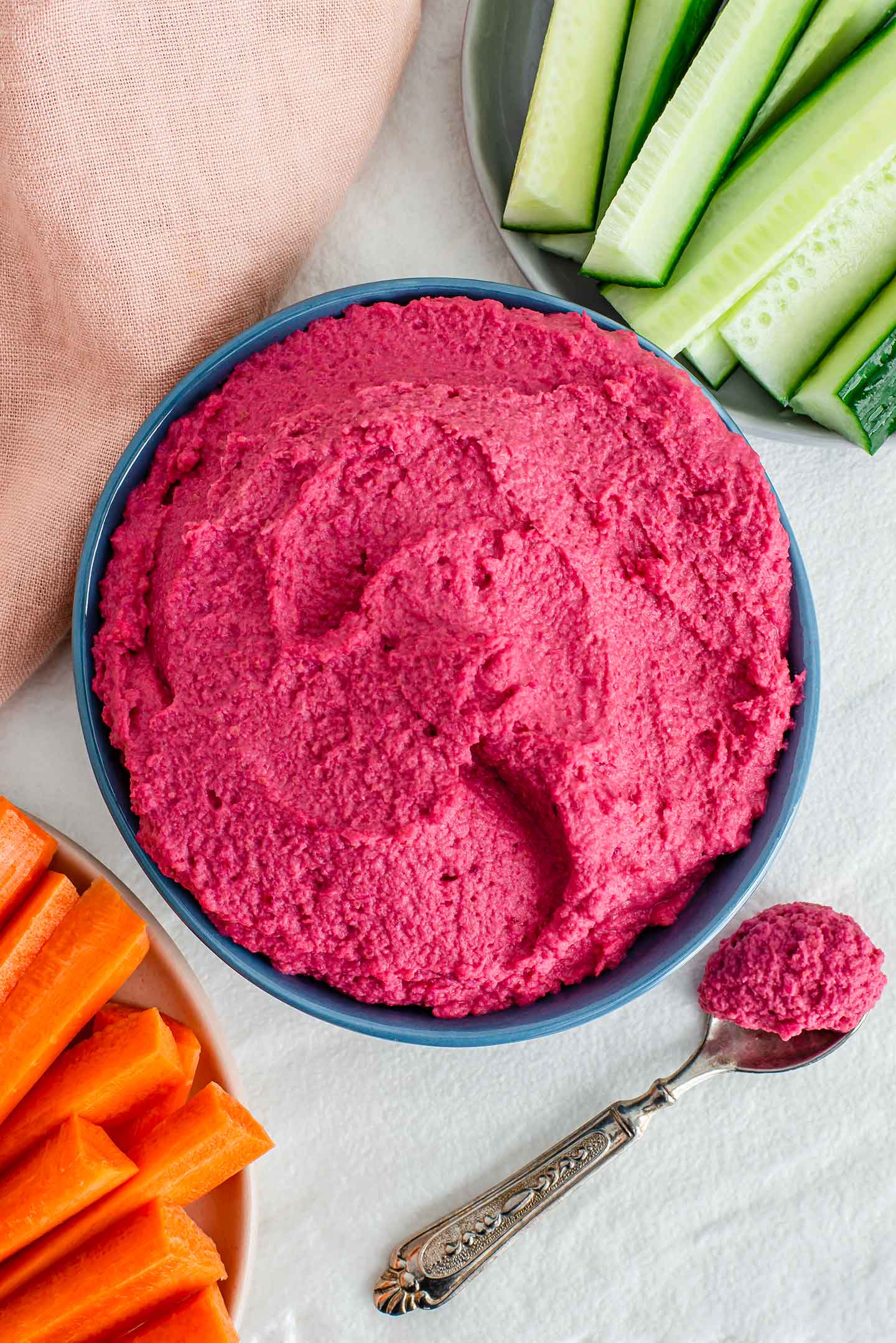 Top down view of a bowl filled with bright pink roasted beet hummus. Carrots and celery sticks surround the bowl.