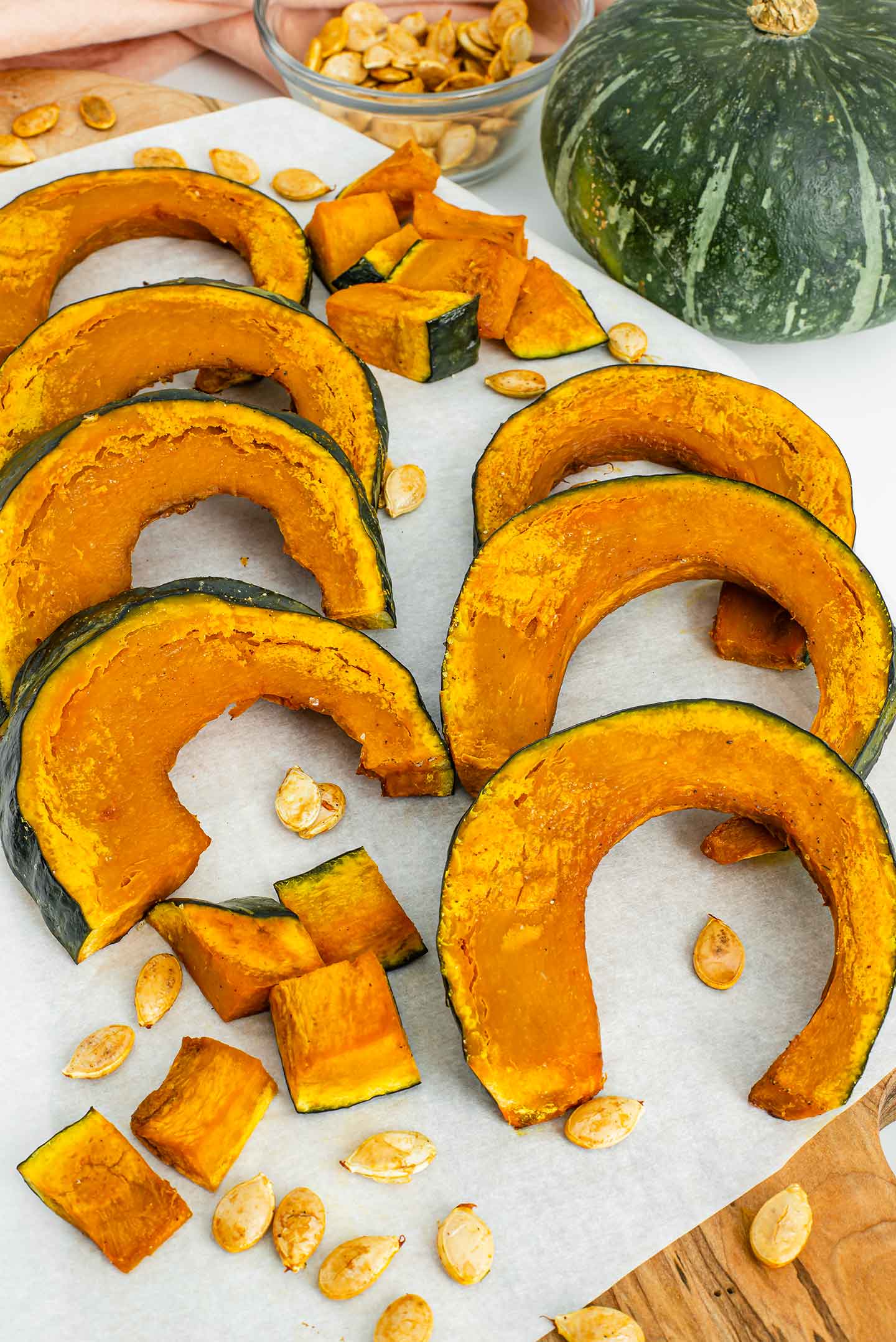 Sliced roasted kabocha squash lines a white tray. A small whole kabocha squash is pictured to show its green colour, and squat shape.