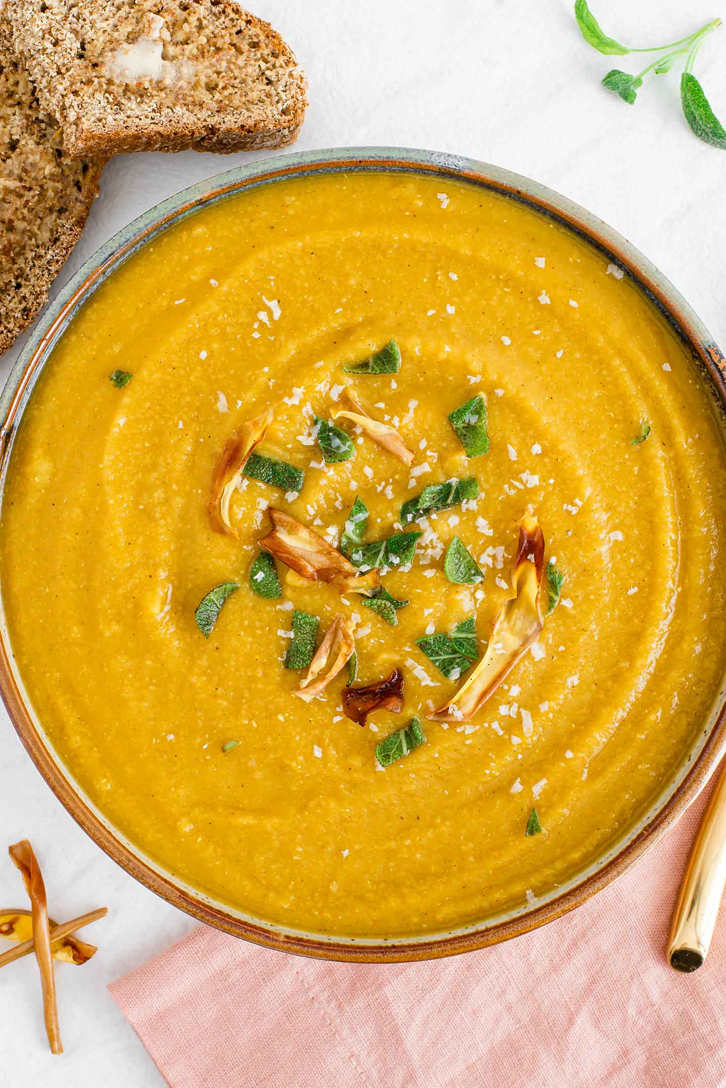 Top down view of a thick and creamy butternut squash red lentil soup in a bowl. The soup is topped with sage and roasted squash peel.
