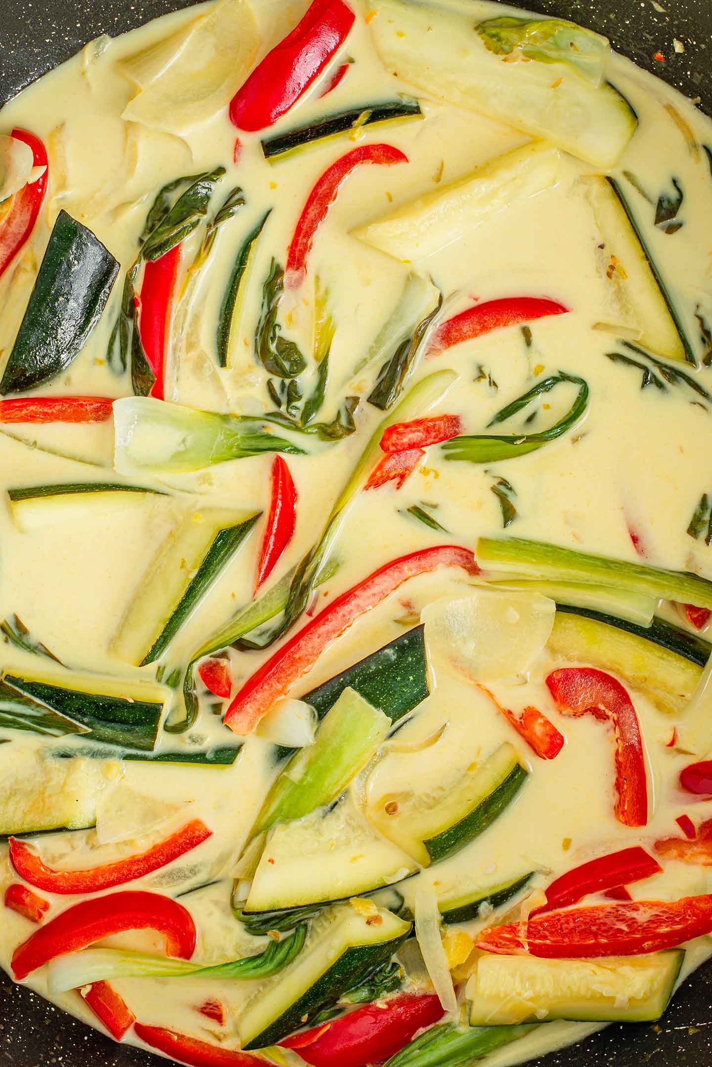 Top down view of a creamy sauce with softened zucchini, red peppers, and bok choy.