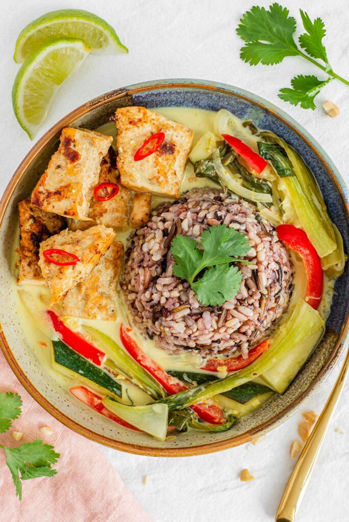 Top down view of chunky coconut lime tofu in a dish with a mound of brown rice and vegetables in a creamy coconut sauce.