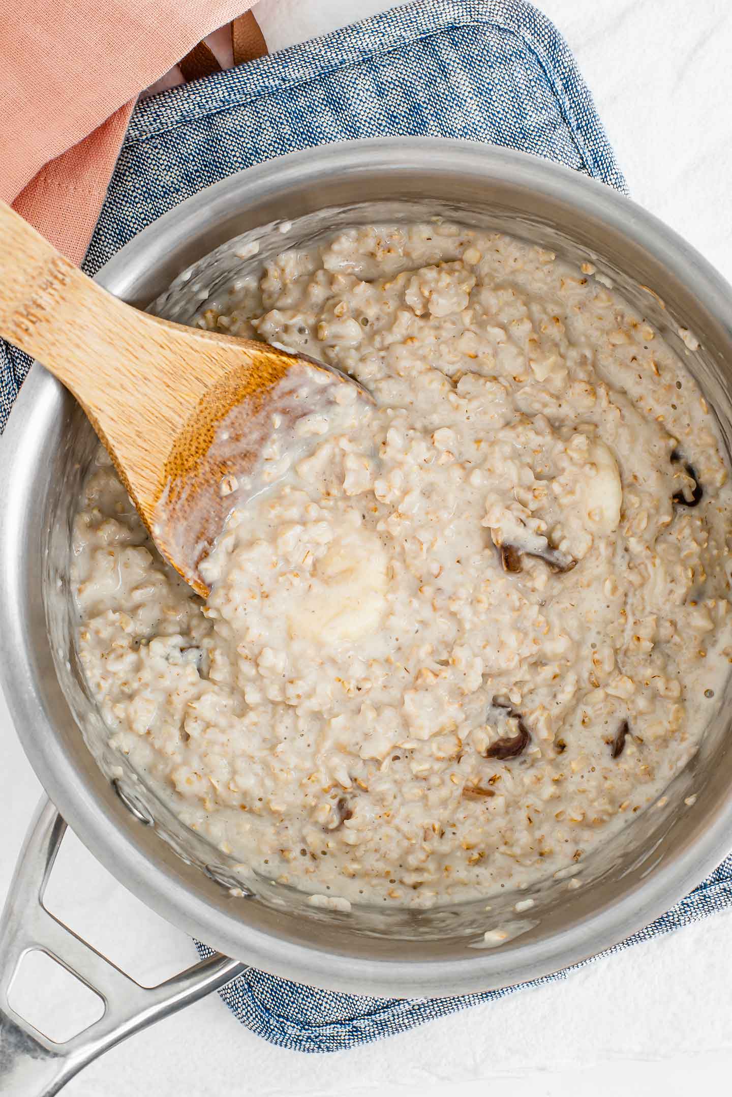 Top down view of a wooden spoon resting in creamy cooked oatmeal in a small pot.