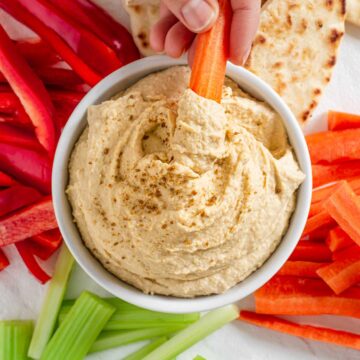 Top down view of a bowl filled with easy creamy homemade hummus. Raw vegetables and naan bread surround the hummus dip.