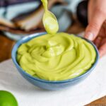 Side view of a bright green creamy avocado lime dressing in a small bowl.