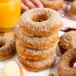 Side view of apple cider doughnuts stacked on a white tray. The top of the doughnuts are sprinkled with cinnamon sugar.