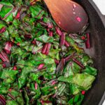 Top down view of cooked beet greens in a cast iron skillet.