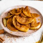 Warm, tender apple slices coated in cinnamon and a dusting of icing sugar are piled on a pink plate.