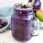 A deep purple blueberry pear smoothie in a glass jar with a handle.