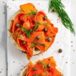 Top down view of open-faced smoky carrot lox breakfast bagel garnished with fresh dill and capers.