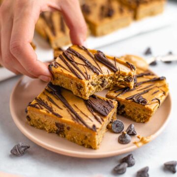 A bite is taken out of a chickpea cookie dough bar drizzled with chocolate and iced with peanut butter.
