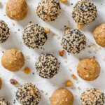 Chickpea tahini protein balls are displayed on a white tray. Some have been rolled in black and white sesame seeds.