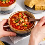 A hand dips a wooden spoon into a comforting bowl of chipotle two bean chilli.