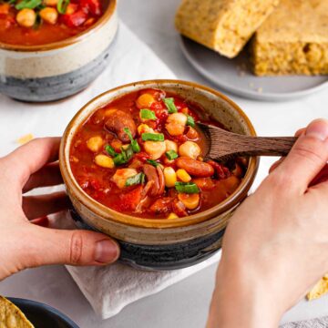 A hand dips a wooden spoon into a comforting bowl of chipotle two bean chilli.