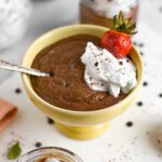 Side view of quick chocolate chia pudding filling a sorbet bowl with a dollop of whipped cream and a fresh strawberry.