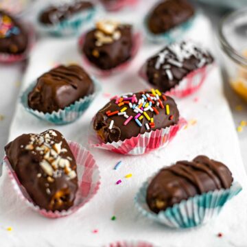 Chocolate covered peanut butter dates with various toppings cover a white tray.