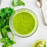 Bright green cilantro lime vinaigrette fills a small dish. Fresh cilantro and lime are nearby.
