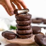 Side view of a stack of peppermint patties. A bite is missing from the top patty showing the thick coconut centre.