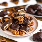 A plate piled high with homemade chocolate turtles. Pecans are topped with a date caramel and a chocolate coating.