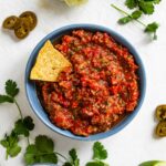 Top down view of easy grape tomato salsa in a shallow dish with a tortilla chip resting in the salsa.