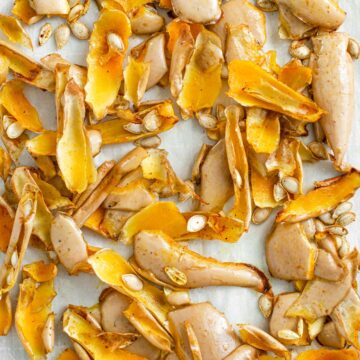 Top down view of roasted squash seeds and skin on a baking tray. The slices of squash peel are curled and toasted.