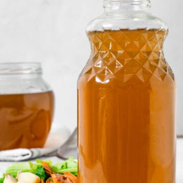 Homemade vegetable broth fills a large glass jar with vegetable scraps to the side.