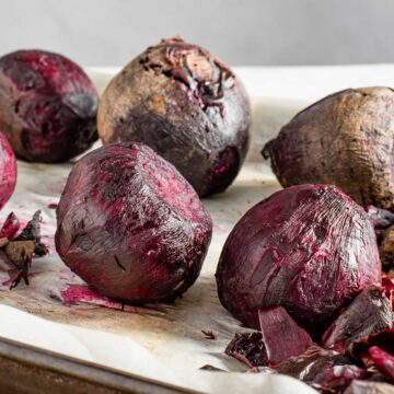 Roasted beets on a baking tray. Some have been peeled and others still have the skin on.