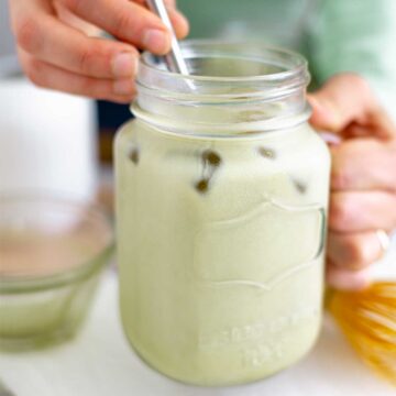 Side view of a hands picking up a dewy glass mug of an iced matcha latte.