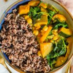 Top down view of a creamy kabocha squash curry with chickpeas, and spinach alongside wild rice.