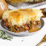 Gravy pours over a slice of sturdy vegan lentil shepherd's pie topped with golden mashed potatoes.